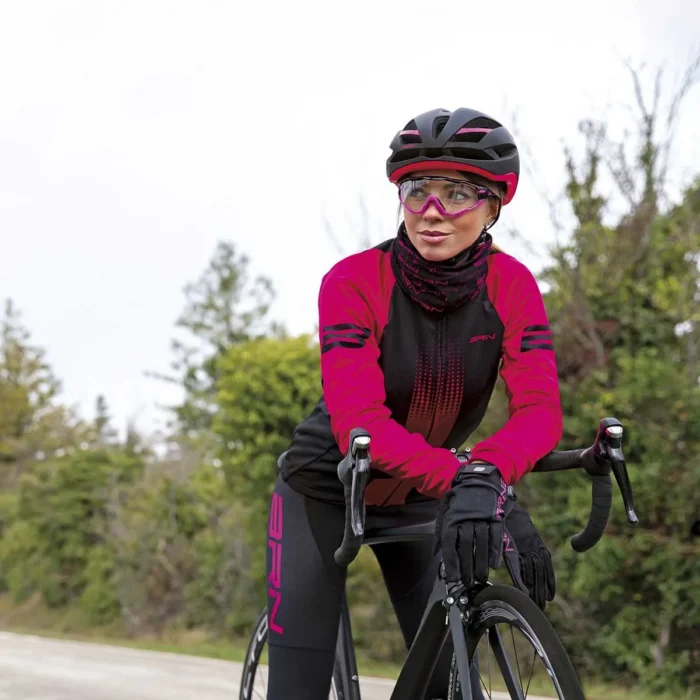 Ciclista donna in maglia BRN a manica lunga, indossando occhiali da sole e casco, pronta per una pedalata all'aperto.