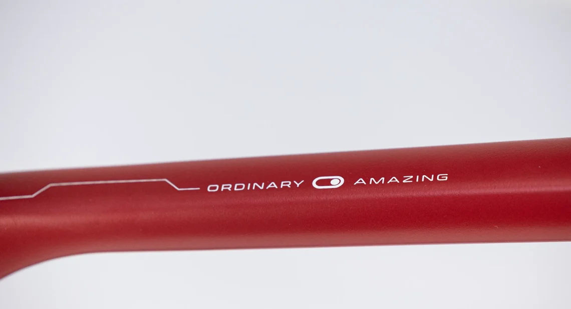 Dettaglio di un tubo di bicicletta rosso con la scritta 'ORDINARY AMAZING', evidenziando il design elegante e moderno