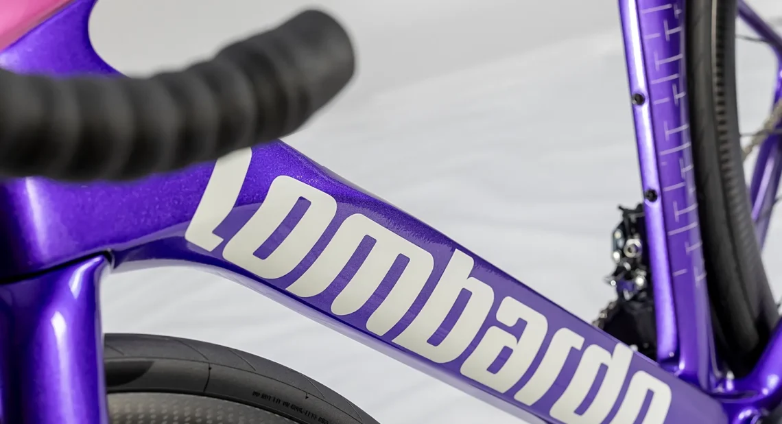Dettaglio del telaio della bicicletta Lombardo, evidenziando il design elegante in colore viola e il logo bianco. Mostra la cura dei dettagli e la qualità dei materiali utilizzati nella costruzione.