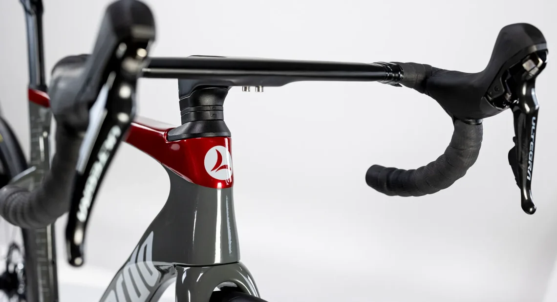 Dettaglio del manubrio della bicicletta Lombardo Misano, evidenziando il design elegante e i componenti di alta qualità. Mostra il telaio in grigio e il logo rosso, insieme ai freni Shimano Ultegra.