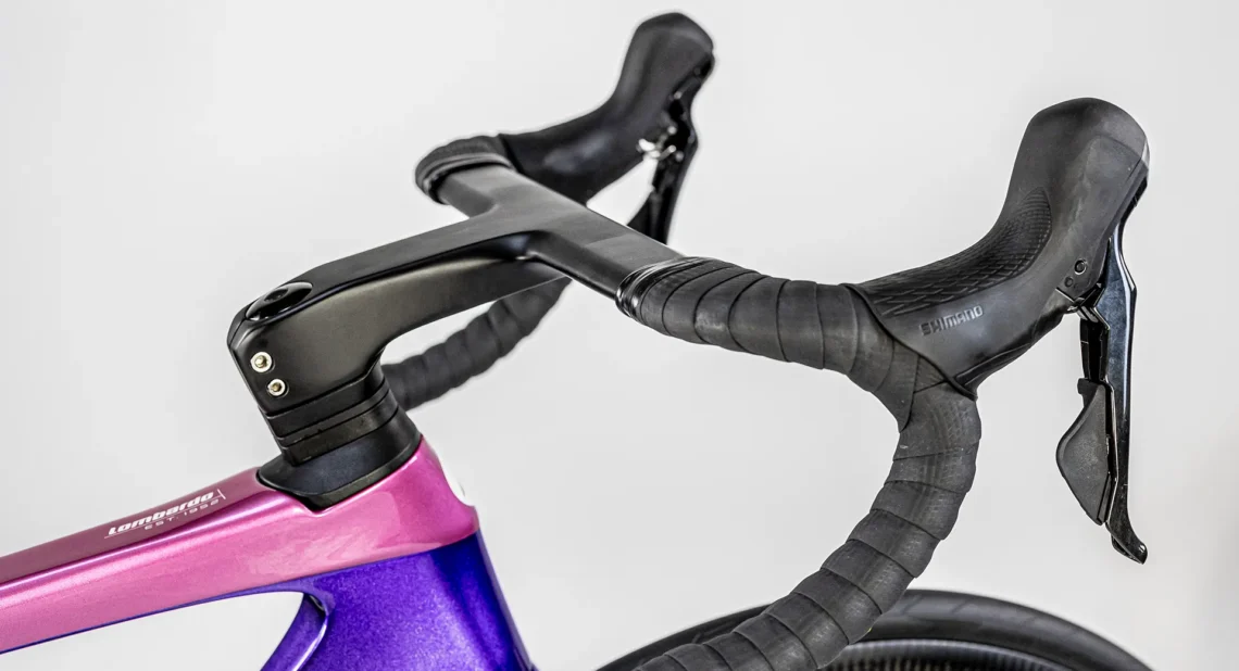 Dettaglio del manubrio della bicicletta Lombardo Misano, mostrando il design elegante con il telaio viola e i freni Shimano. Il manubrio nero offre una presa sicura per una guida confortevole.